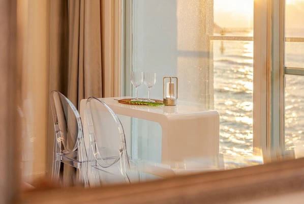 Una mesa con dos copas de vino y una vela, frente a una ventana con vistas al mar.