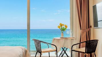 A hotel room with a large window, a bed, two chairs, a small table with a vase of flowers, and a TV on the wall.