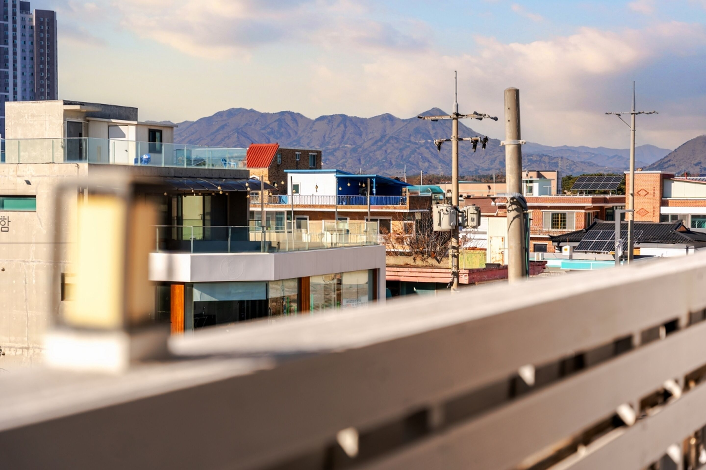 A modern building with a glass facade, a red-roofed structure, and a mountain range in the background.