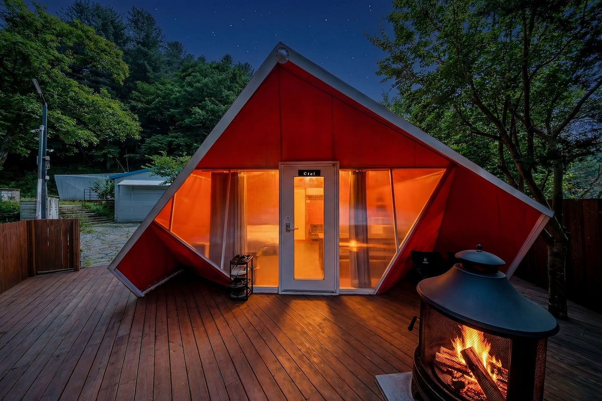 Une tente triangulaire avec une porte portant l’inscription « Ciel » et un foyer à l’extérieur.