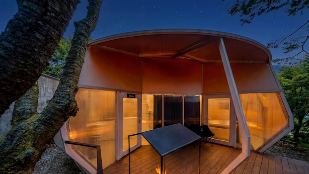 Una estructura circular moderna al aire libre con un hogar en el centro, una mesa y un banco.