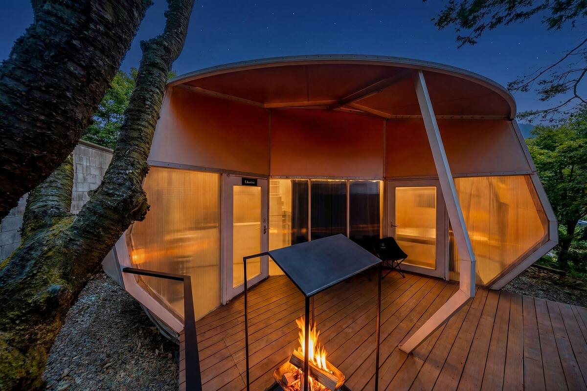 Une structure extérieure moderne et circulaire, avec un foyer au centre, une table et un banc.