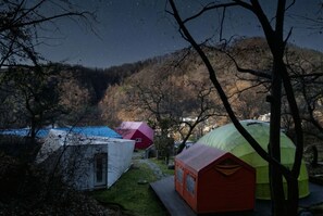 A campsite with various dome-shaped tents and a small white building, surrounded by trees and hills.