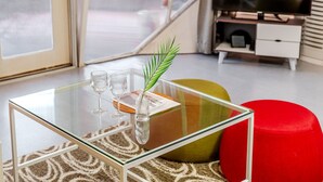 Una sala de estar moderna con una mesa de centro de vidrio, un otomán rojo y una alfombra estampada.