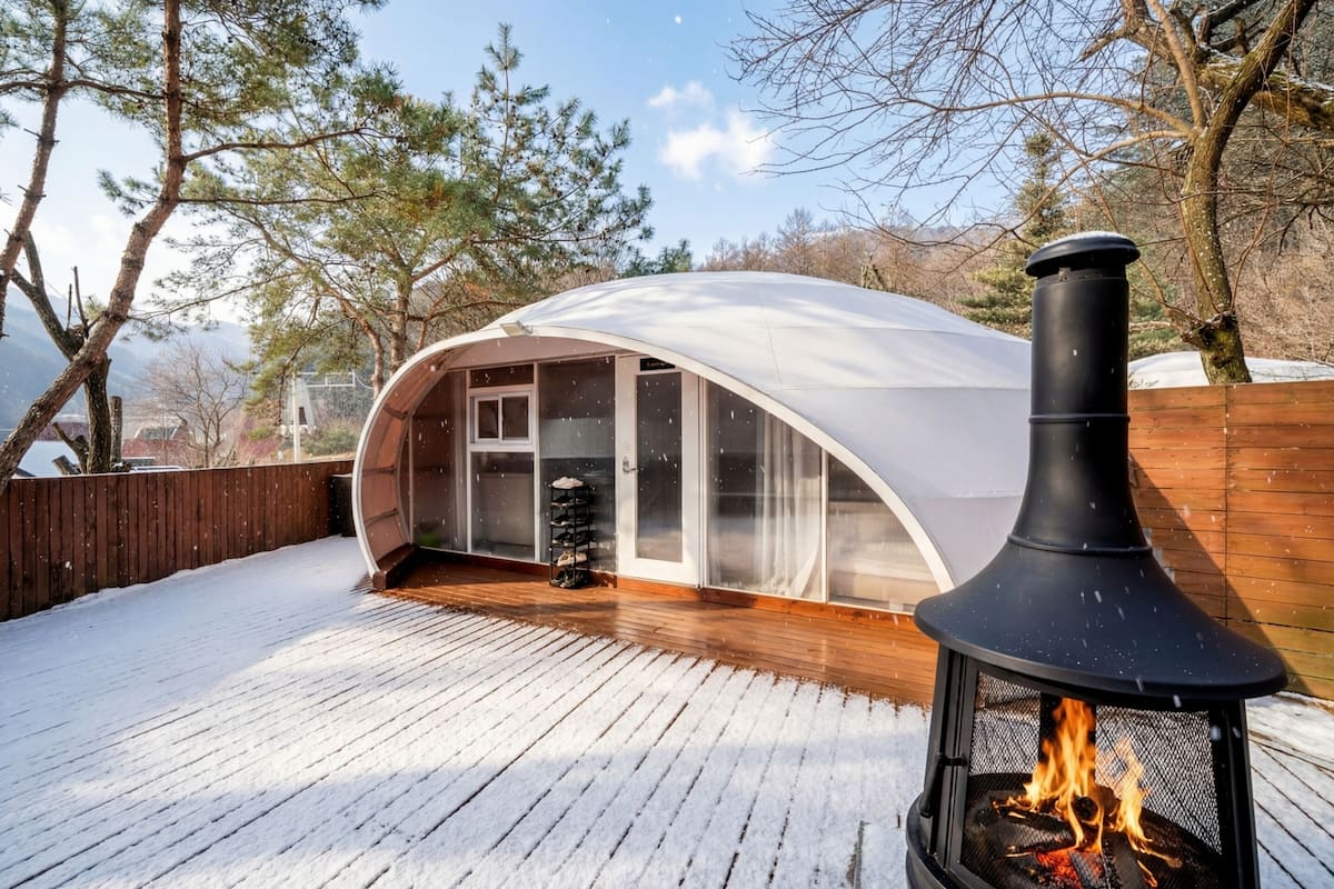 Une terrasse enneigée, surmontée d’une structure fermée par des parois de verre et agrémentée d’une cheminée noire.