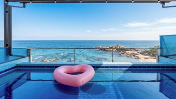 Una piscina con un flotador con forma de corazón, agua azul cristalina y vistas al océano y la costa rocosa.