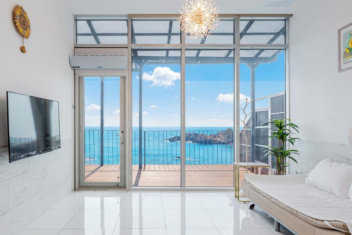 Une chambre moderne dotée d’une grande porte-fenêtre coulissante donnant sur un balcon avec vue sur la mer.