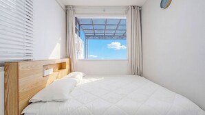 A bedroom with a wooden headboard, a bed with white bedding, a window with a view of the sky, and a wall clock. - Yeongdeok Searest Poolvilla (Yeongdeok)