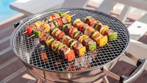 Un barbecue extérieur rond, en acier inoxydable, avec des brochettes de viande et de légumes.