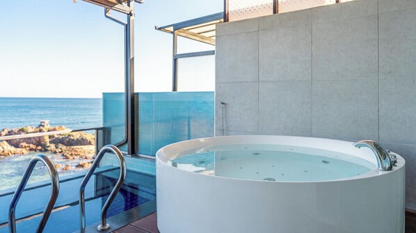 Une salle de bain moderne dotée d’une grande baignoire, d’une douche séparée par des parois en verre et offrant une vue sur l’océan.