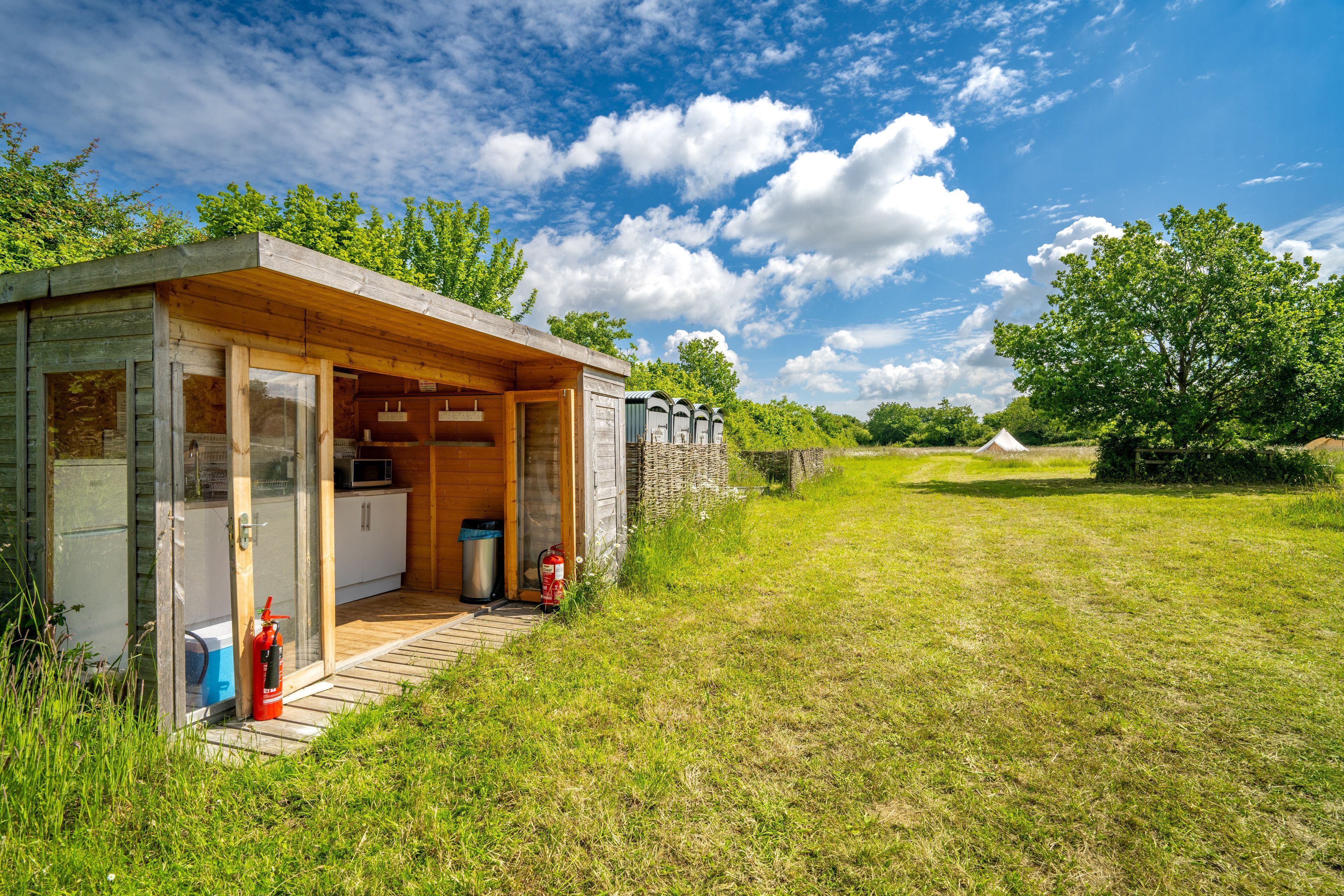 A modern wooden cabin with a glass door entrance, a small porch, and a fire extinguisher outside.