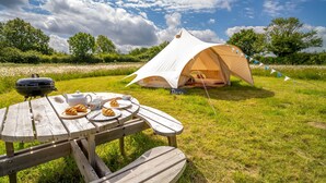 A picnic setup with a tent labeled "Daisy," a wooden table with croissants, a kettle, and a plate of food. - Glamping accommodation in Norfolk, Blancas Bell Tents sleeps up to 20 people. (Ringstead)