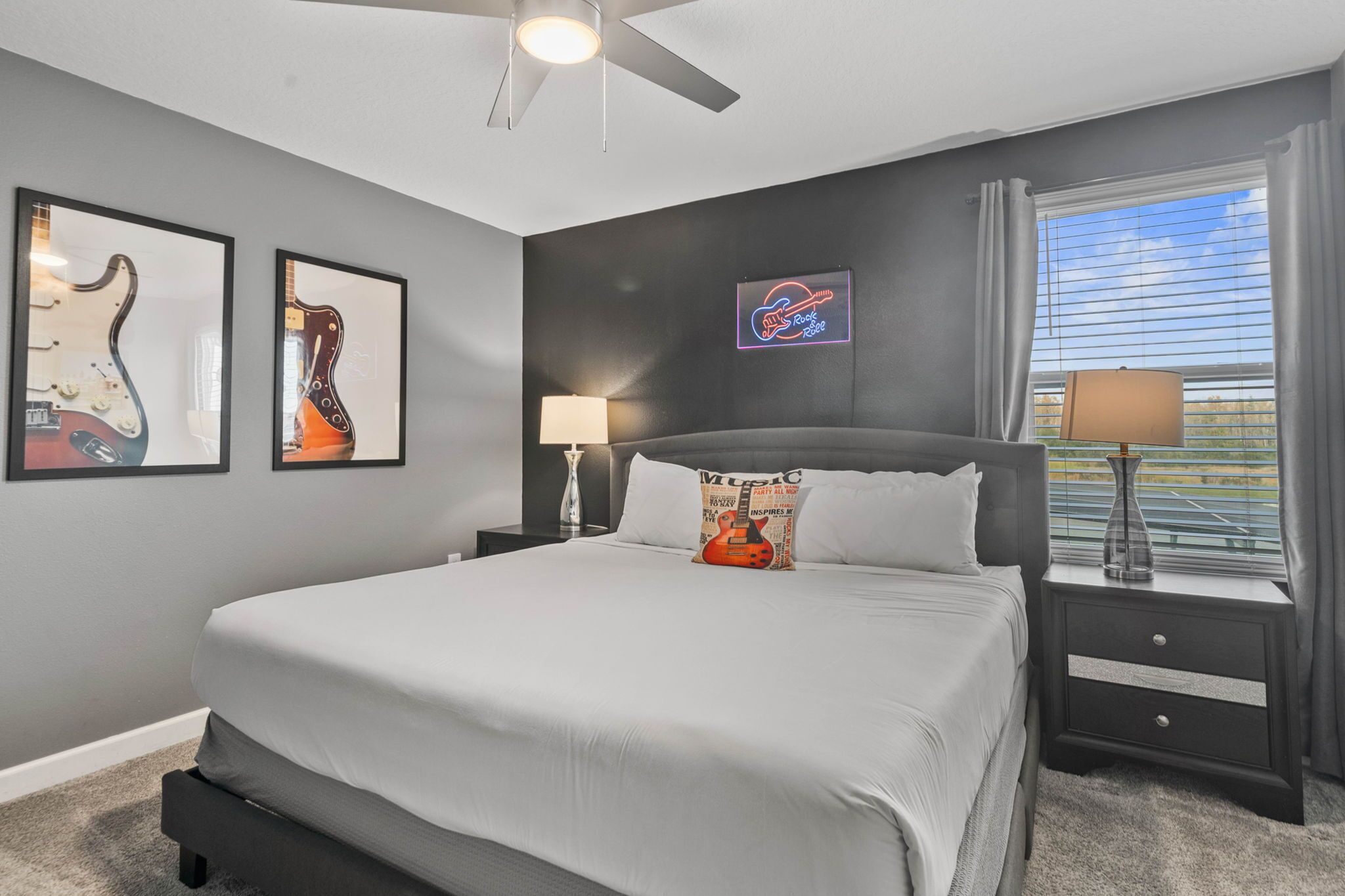 A bedroom with a bed, two nightstands, a ceiling fan, framed guitars, and a window with curtains.