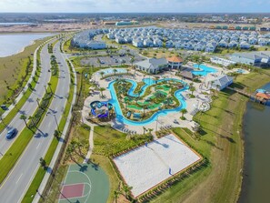 Una vista aerea di una zona residenziale con un complesso piscine, un campo da basket e una strada con veicoli.