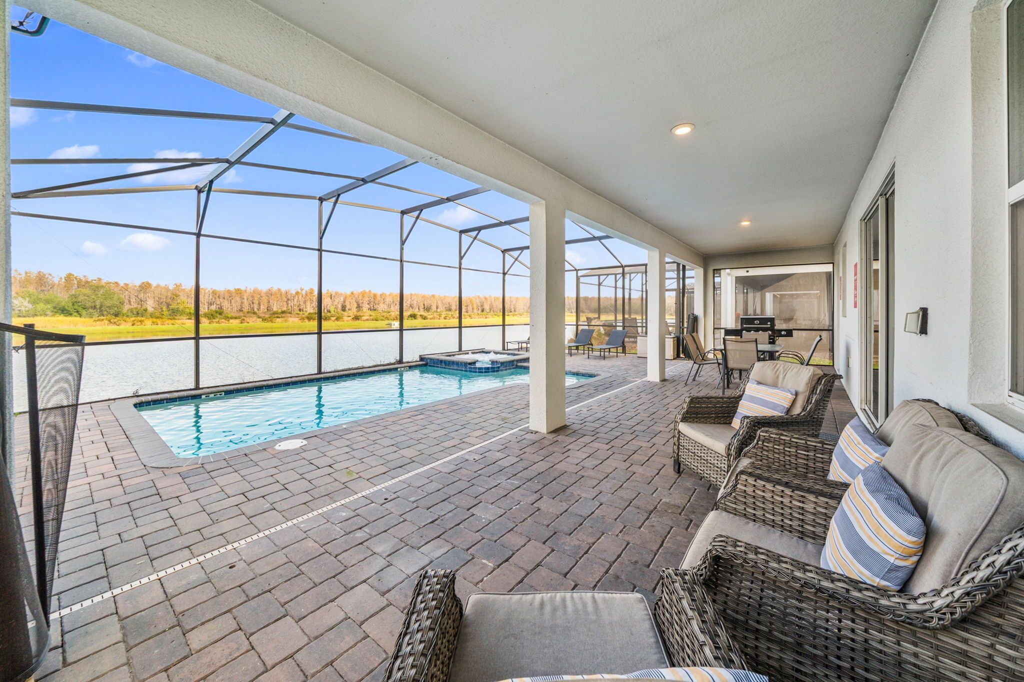 A covered outdoor area with a pool, wicker furniture, and a view of a lake.