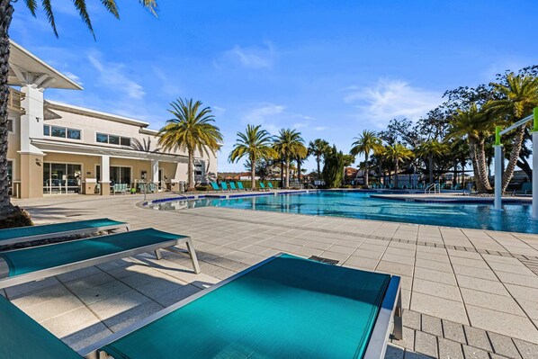 A swimming pool with lounge chairs, palm trees, and a modern building. - 4449 Shiva Loop (Kissimmee)