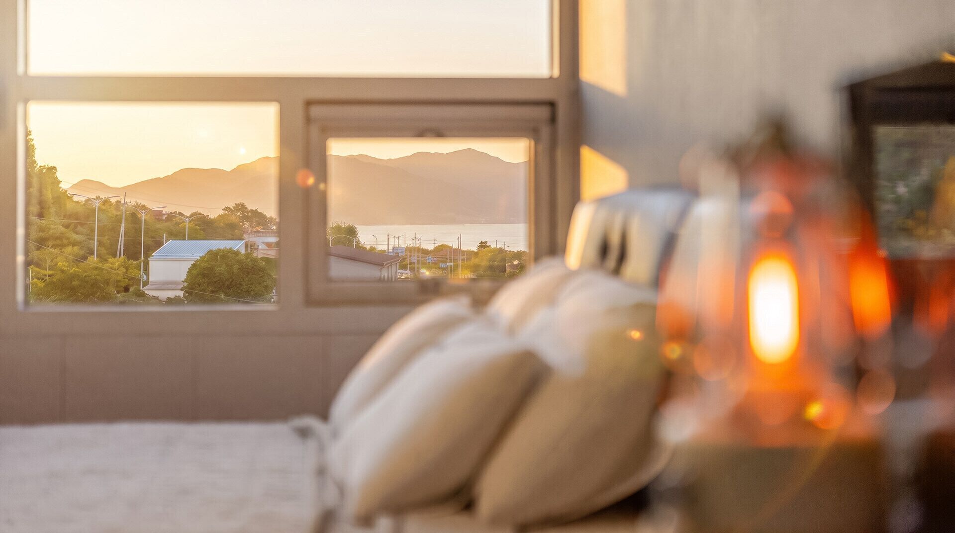 A room with a bed, pillows, a window, and a view of mountains and a body of water.