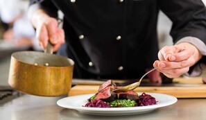 Een kok bereidt een gerecht met steak en groenten op een bord.