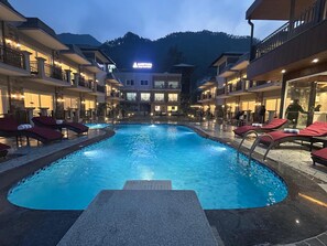 Een zwembadgedeelte van een hotel met ligbedden en uitzicht op de bergen.
