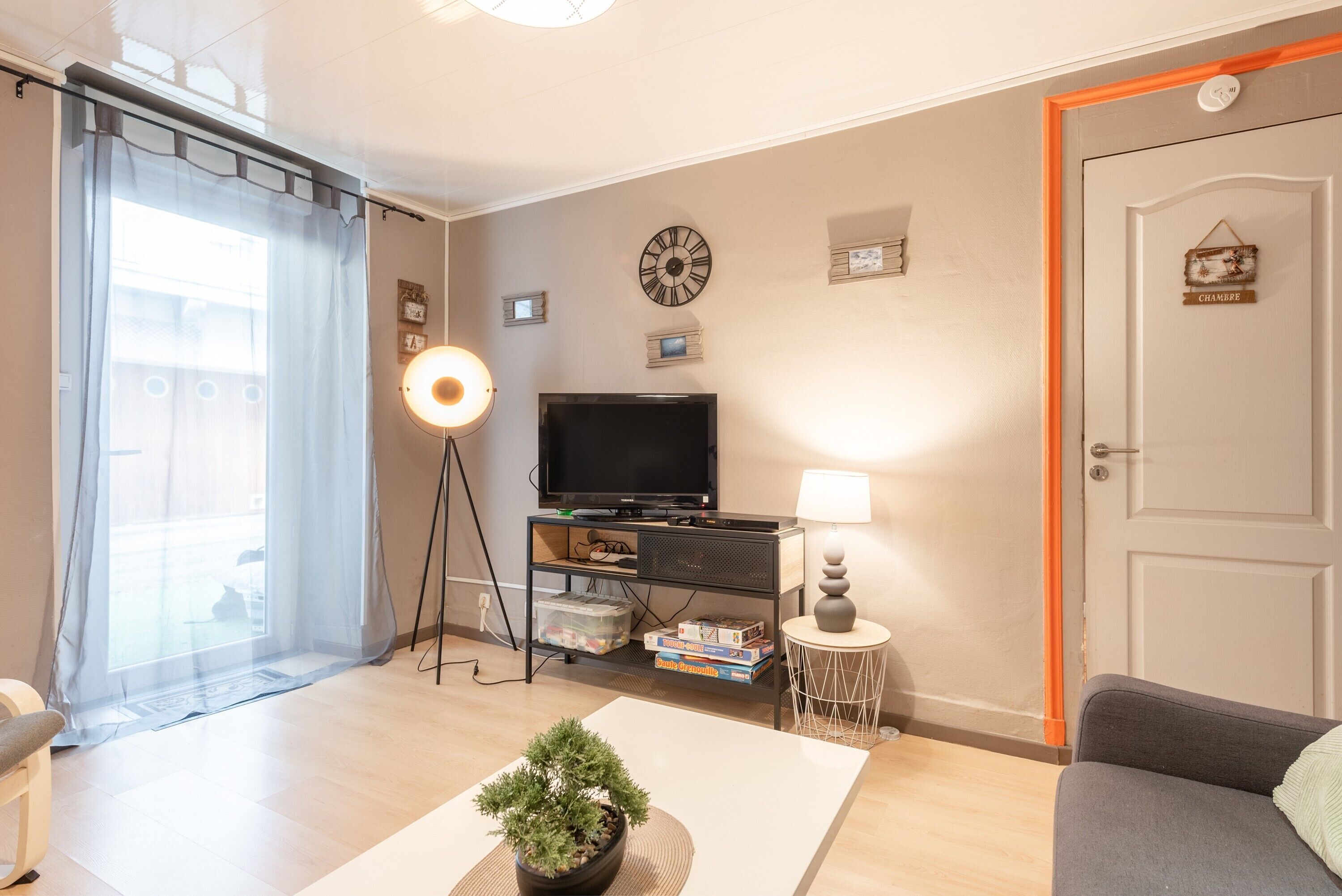 Una sala de estar con televisión, lámpara, reloj y una puerta con un letrero.