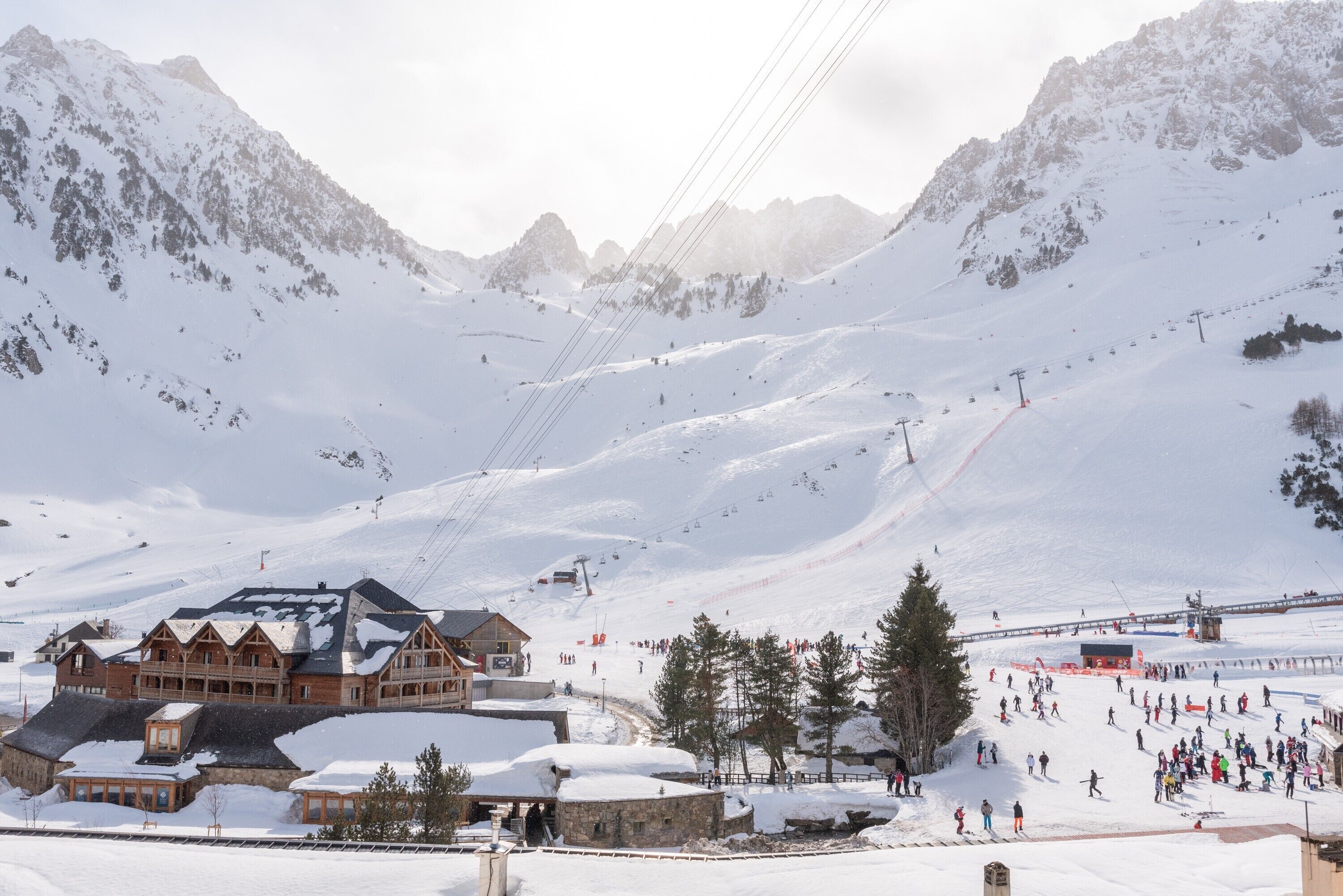 Ein schneebedecktes Bergresort mit Seilbahn, Holzhäusern und Skipiste.