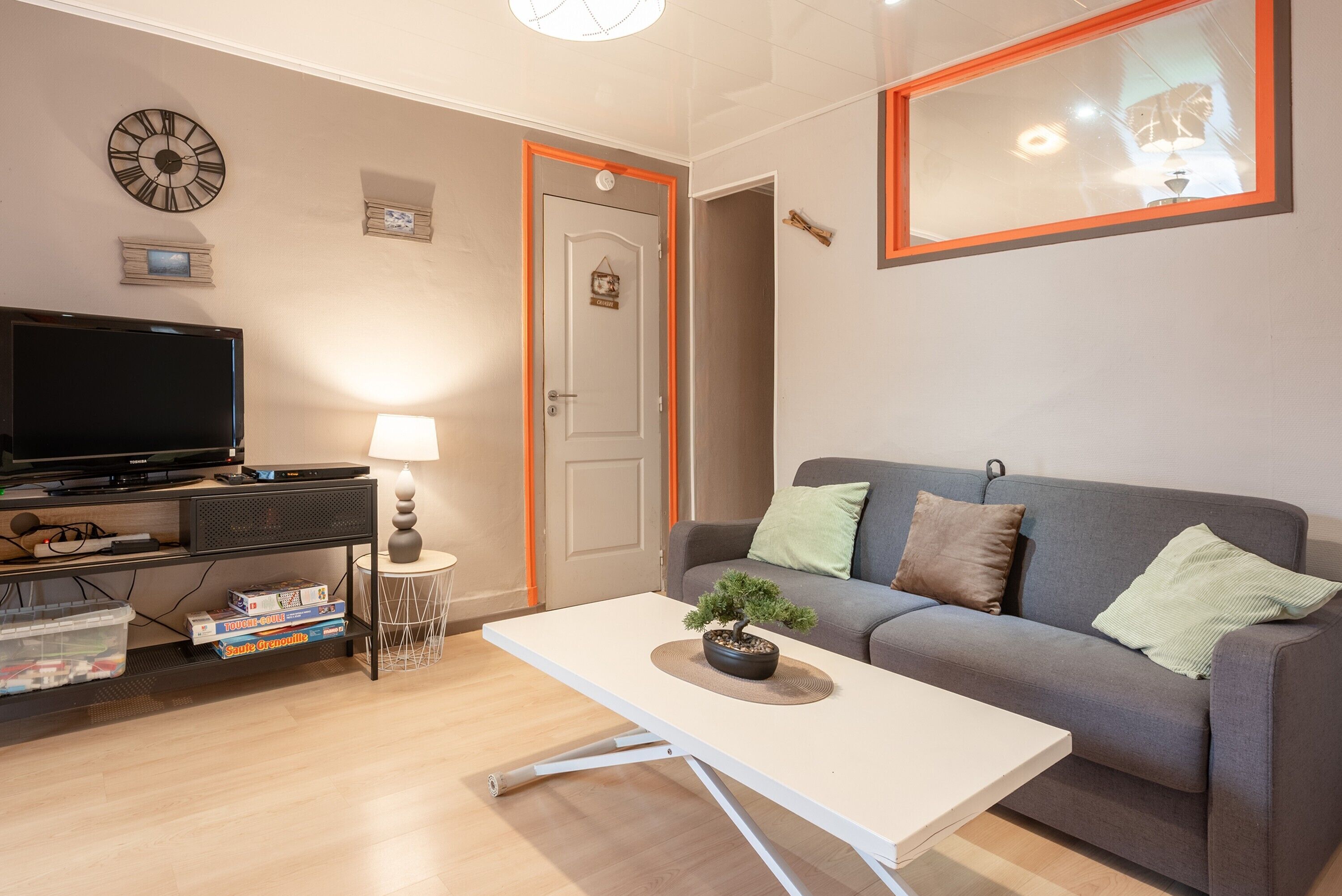 A living room with a sofa, a coffee table, a TV, and a clock on the wall.