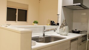 A modern kitchen with a stainless steel sink, white cabinets, and a window above the sink. - Shibuya Honcho household cell (渋谷区)