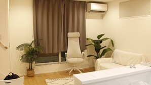 A modern hotel room with a large window, a white desk, a white chair, a sofa, and a potted plant. - Shibuya Honcho household cell (渋谷区)