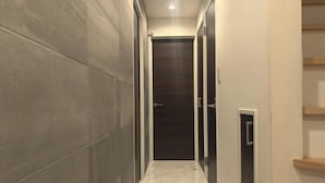 A narrow hallway with tiled walls and a dark wooden door at the end. - Shibuya Honcho household cell (渋谷区)