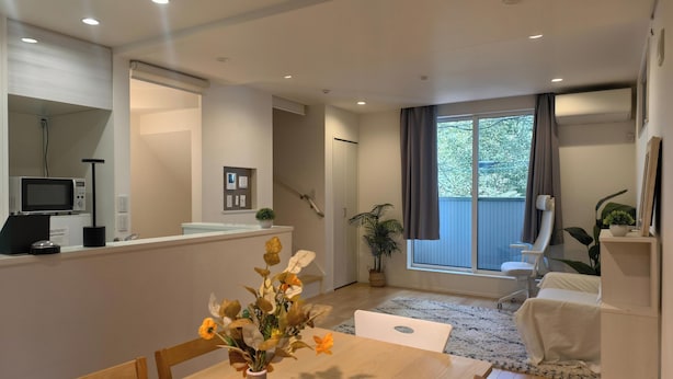 A modern living room with a dining area, a large window with curtains, a microwave, and a small plant on the counter. - Shibuya Honcho household cell (渋谷区)
