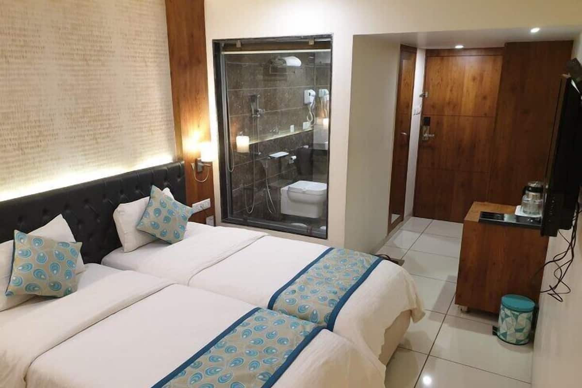 A hotel room with a bed, a bathroom with a glass shower enclosure, and a wooden wardrobe.