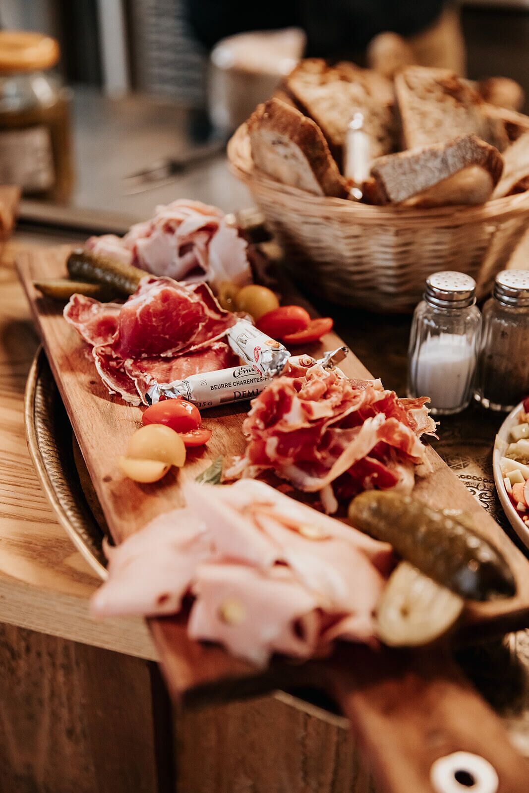 A wooden board with various meats, pickles, and bread.