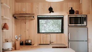 A compact kitchen with wooden walls, a window, a microwave, and a refrigerator. - Domaine Saint-Amand (Saint-Amand-de-Coly)