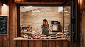 A restaurant counter with a menu board, a woman serving food, and a brick wall interior. - Domaine Saint-Amand (Saint-Amand-de-Coly)