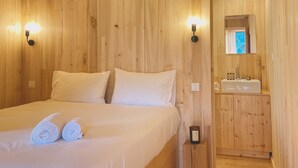 A wooden-paneled room with a bed, two wall sconces, a nightstand, and a wooden cabinet with a mirror.