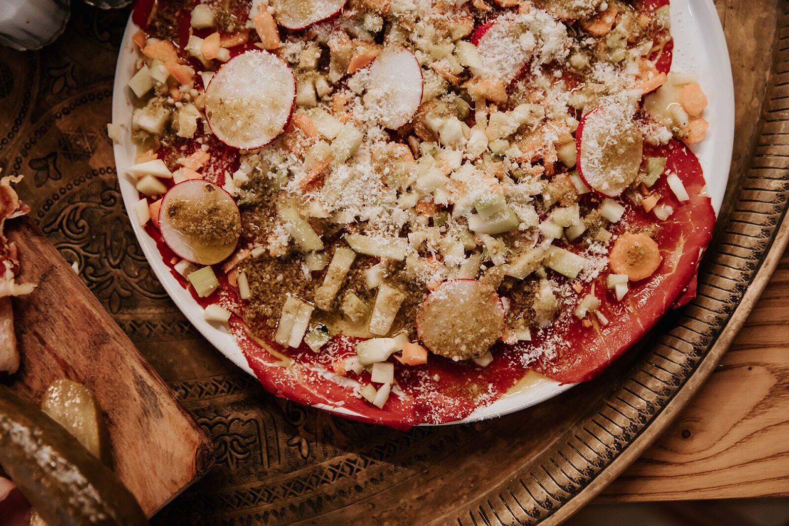 A pizza with various toppings on a white plate, placed on a wooden tray.