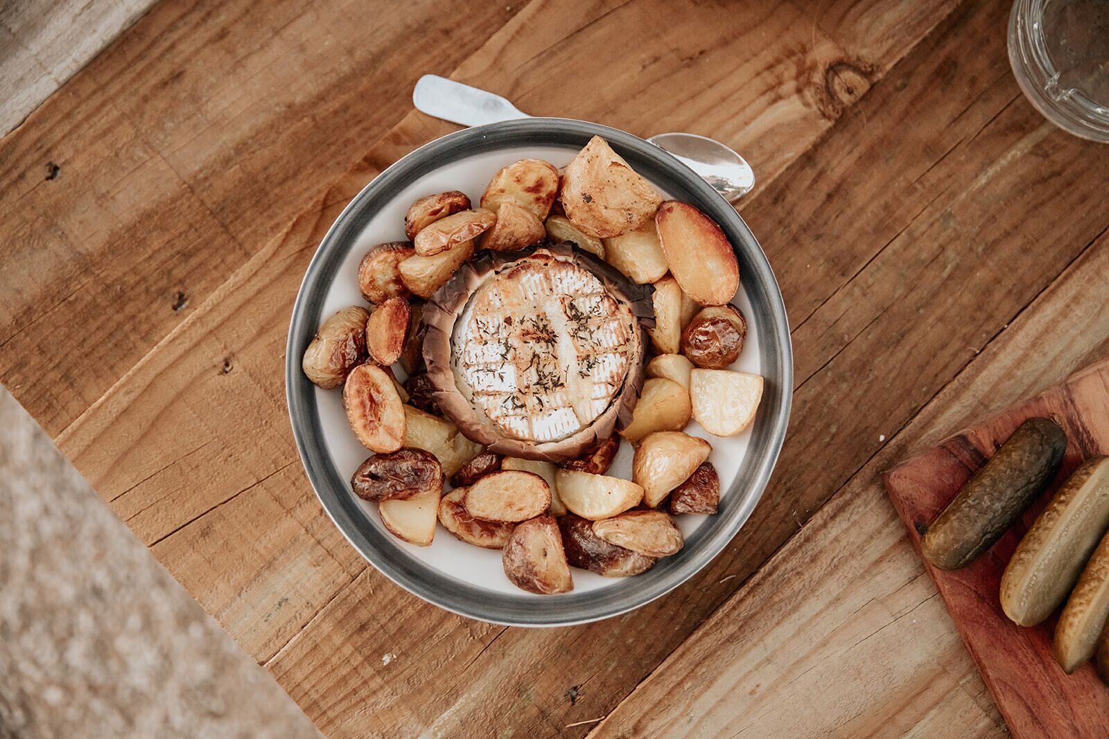 A bowl of roasted potatoes and a grilled cheese sandwich on a wooden table.