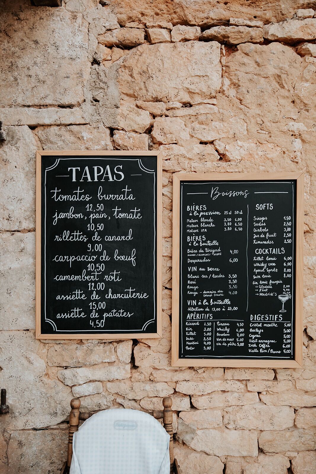 Two blackboards with food and drink menus against a stone wall.