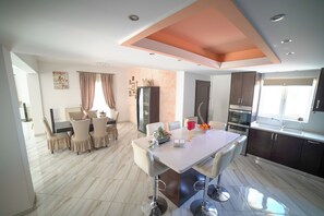 A modern kitchen with a central island, dark cabinets, and a large window. - Villa Thea (Moires)
