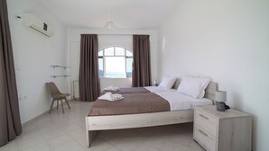 Ein Schlafzimmer mit zwei Betten, einem Sessel, einem Nachttisch und einem Fenster mit Vorhängen.