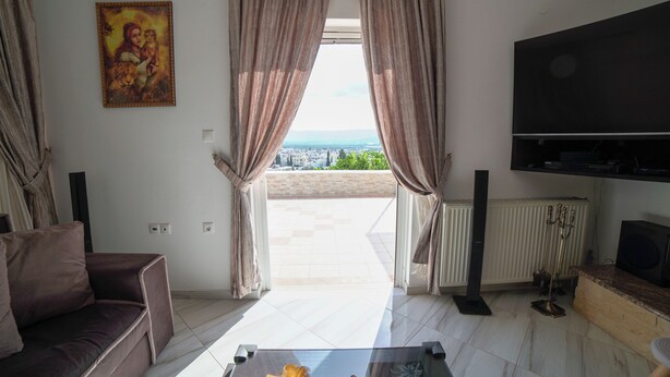 Ein Wohnzimmer mit einer Couch, einem Couchtisch, einem Fernseher und Blick durch Vorhänge auf einen Außenbereich.