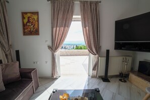 Un salon comprenant un canapé, une table basse, un téléviseur et une vue sur l’extérieur, visible à travers les rideaux.