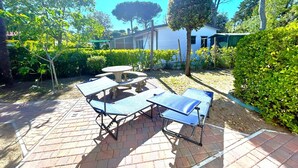 Un patio con tavolo e sedie, immerso nel verde con un edificio sullo sfondo.