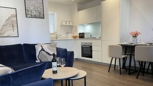 Ett modernt vardagsrum med en blå soffa, ett runt soffbord och en matplats med två stolar och ett litet bord.