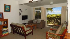 Una sala de estar con sofá, sillones, una mesa de centro, una estantería y televisión.