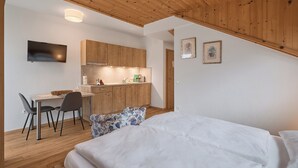 Una habitación moderna con techo de madera, cama, escritorio con sillas, zona de cocina y televisor de pantalla plana.