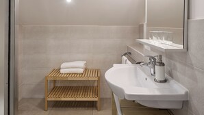 Un baño moderno con un banco de madera, un lavabo blanco y un espejo con iluminación.
