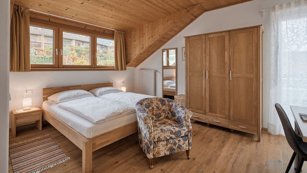 Un dormitorio con techo de madera, una cama, una silla, un armario y una ventana con cortinas.