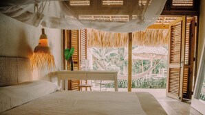 A bedroom with a bed, bedside table, and a view of the outdoors through open shutters. - ¨El Refugio¨3 bedroom bungalow with pool & A/C near Macao beach (Punta Cana)