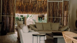 A cozy room with a thatched roof, a sofa, a chair, and a small table. - ¨El Refugio¨3 bedroom bungalow with pool & A/C near Macao beach (Punta Cana)